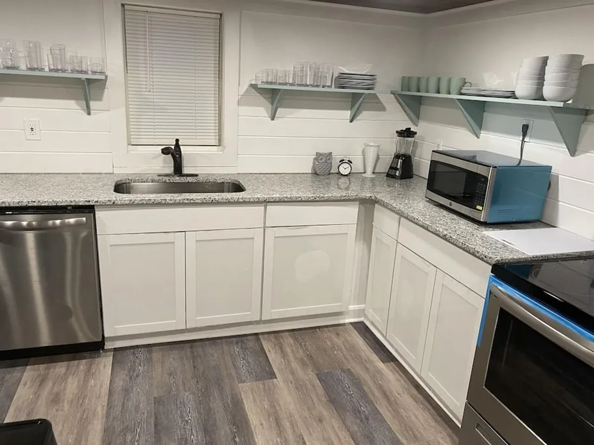 This image showcases the kitchen's stainless steel appliances, a granite countertop, a colorful microwave, and open shelving with neatly arranged dishes. The setup exudes a welcoming and functional atmosphere and highlights an area perfect for both everyday meal prep and lively gatherings.