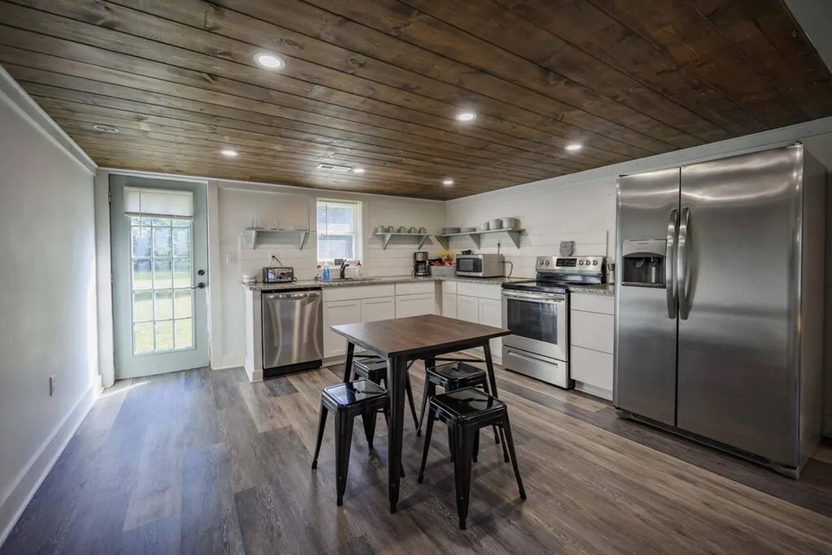 A welcoming kitchen scene displaying a kitchen island, stainless steel appliances, and a wooden ceiling. The setting is both cozy and functional, with clear spaces for cooking, entertaining, and family meals.