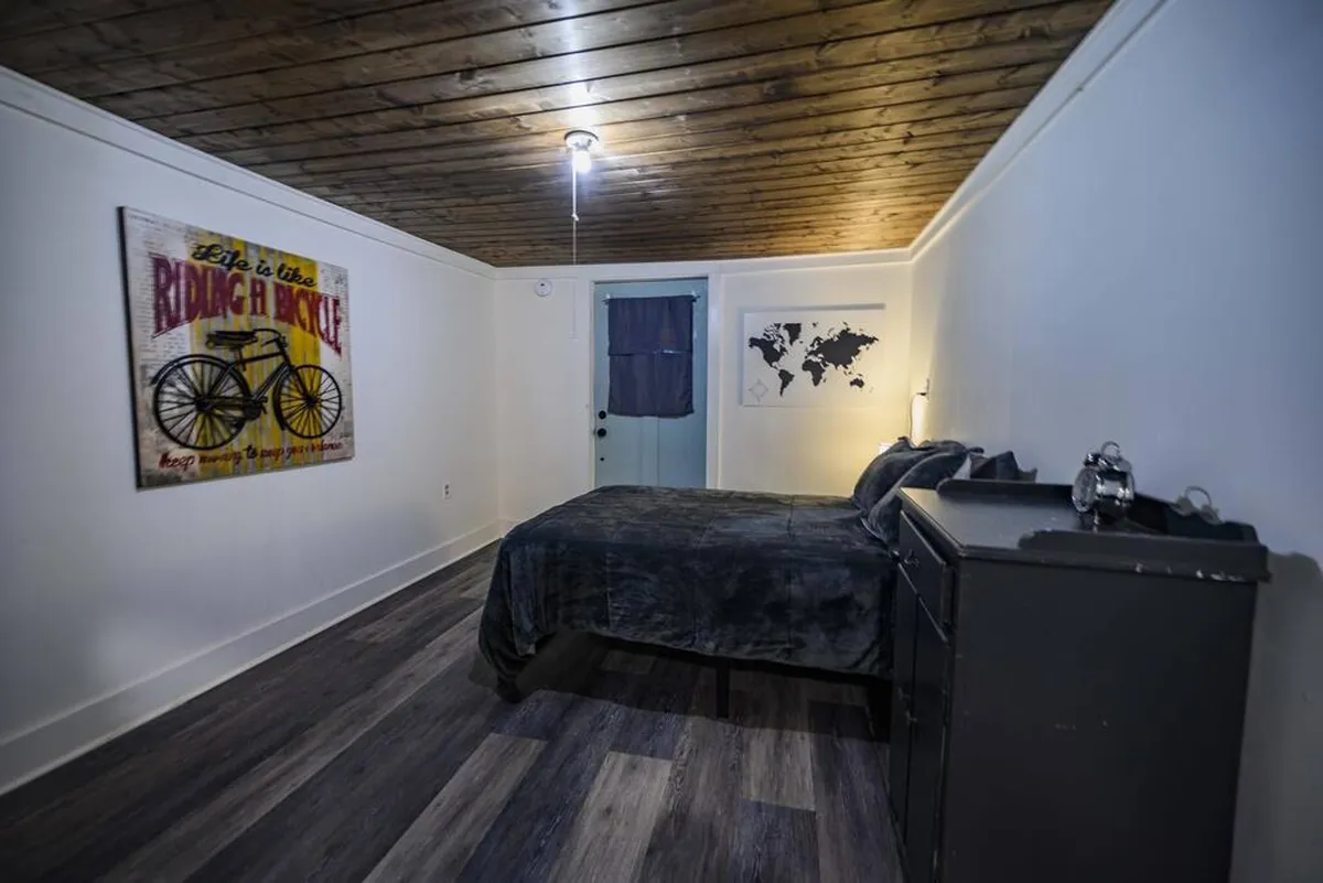A serene bedroom with a plush bed dressed in dark bedding sits against a wall adorned with decorative bicycle art and a large world map. A black dresser adds a modern touch, while the overall decor creates a peaceful, inviting atmosphere ideal for relaxation and restful sleep.