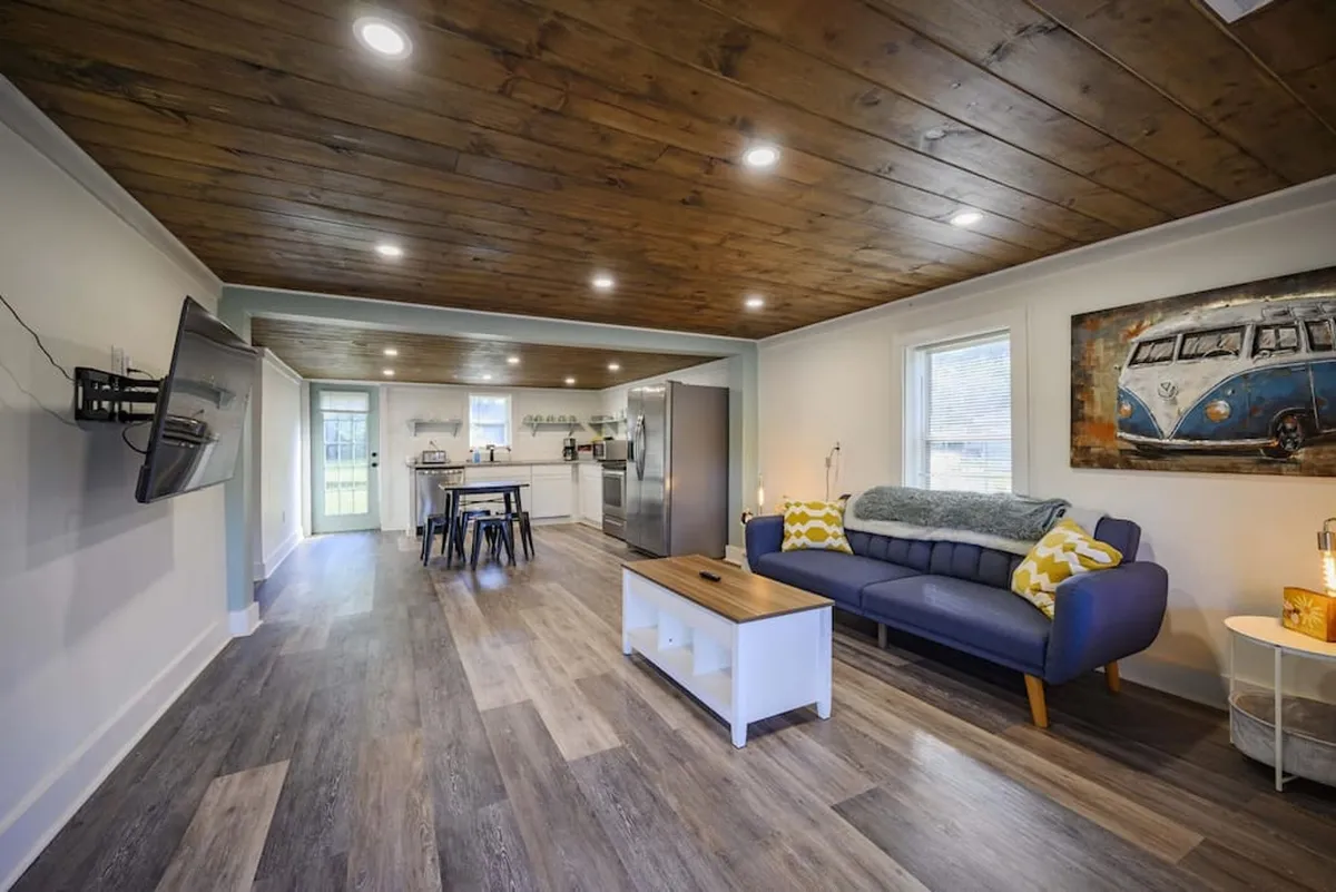 The image showcases a beautifully renovated open-concept living area with a comfortable sofa, stylish coffee table, modern kitchen, and inviting artwork. The space feels welcoming and perfect for relaxing movie nights, cooking together, and spending quality time with loved ones.